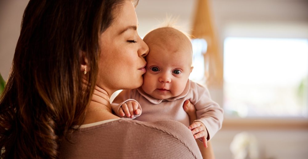 young mother kissing her wide eyed baby